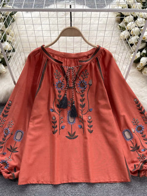 Orange red embroidered tie neck blouse with billowy sleeves and floral details.