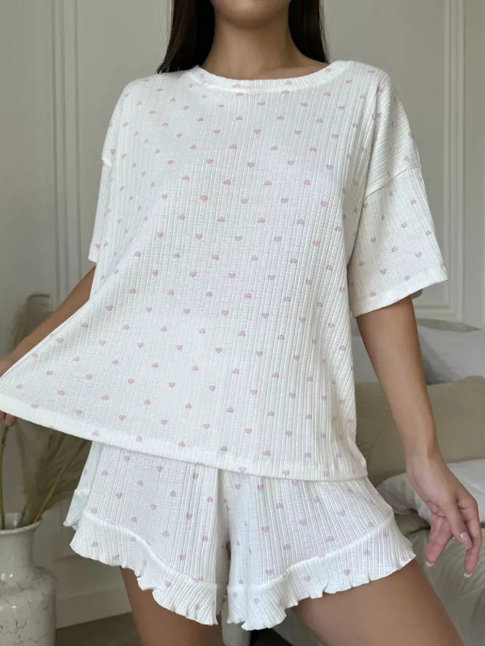 White cotton blend pajama set with pink heart print, featuring a crewneck tee and ruffled shorts.