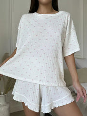 White cotton blend pajama set with pink heart print, featuring a crewneck tee and ruffled shorts.