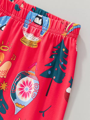 Children's red Christmas pajama set with festive holiday print including penguins in snow globes and ornaments.