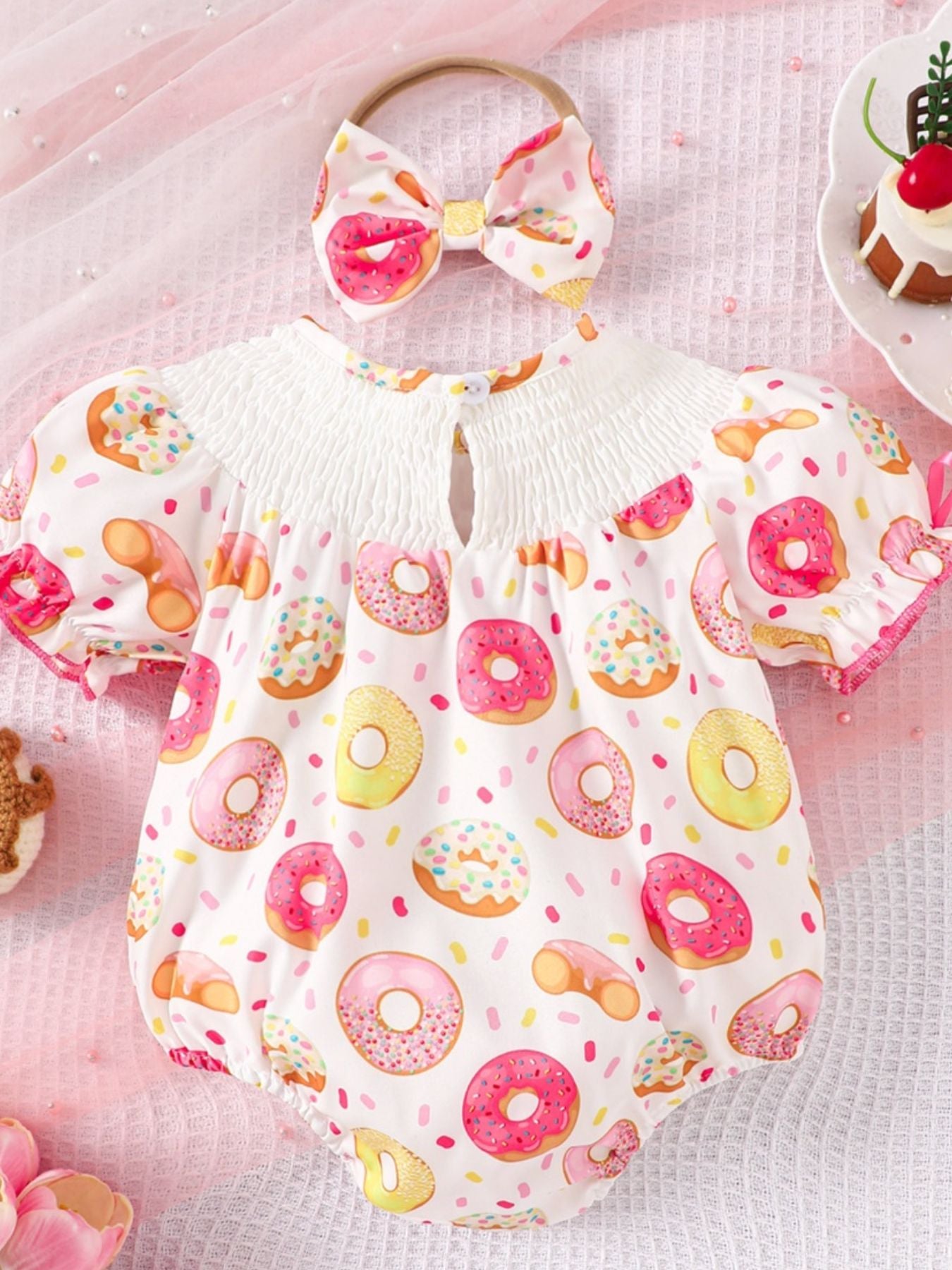 Baby smocked one-piece with donut print, puff sleeves, and matching headband.
