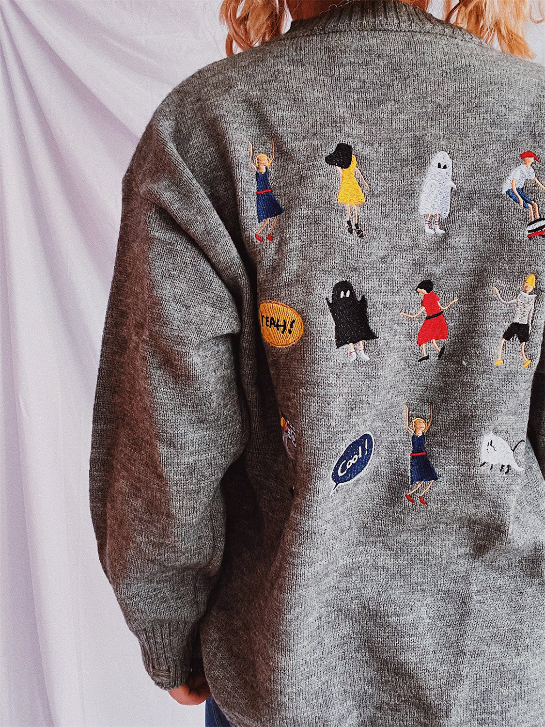 Dark gray knit sweater with embroidered characters and speech bubbles, crew neck, relaxed fit.