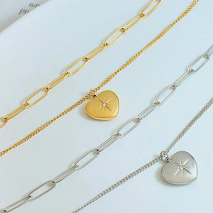 Layered heart pendant necklaces in gold and silver with paperclip chains and starburst detail.