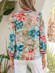 Women's V-neck blouse with a vibrant floral print, striped cuffs, and puff sleeves.