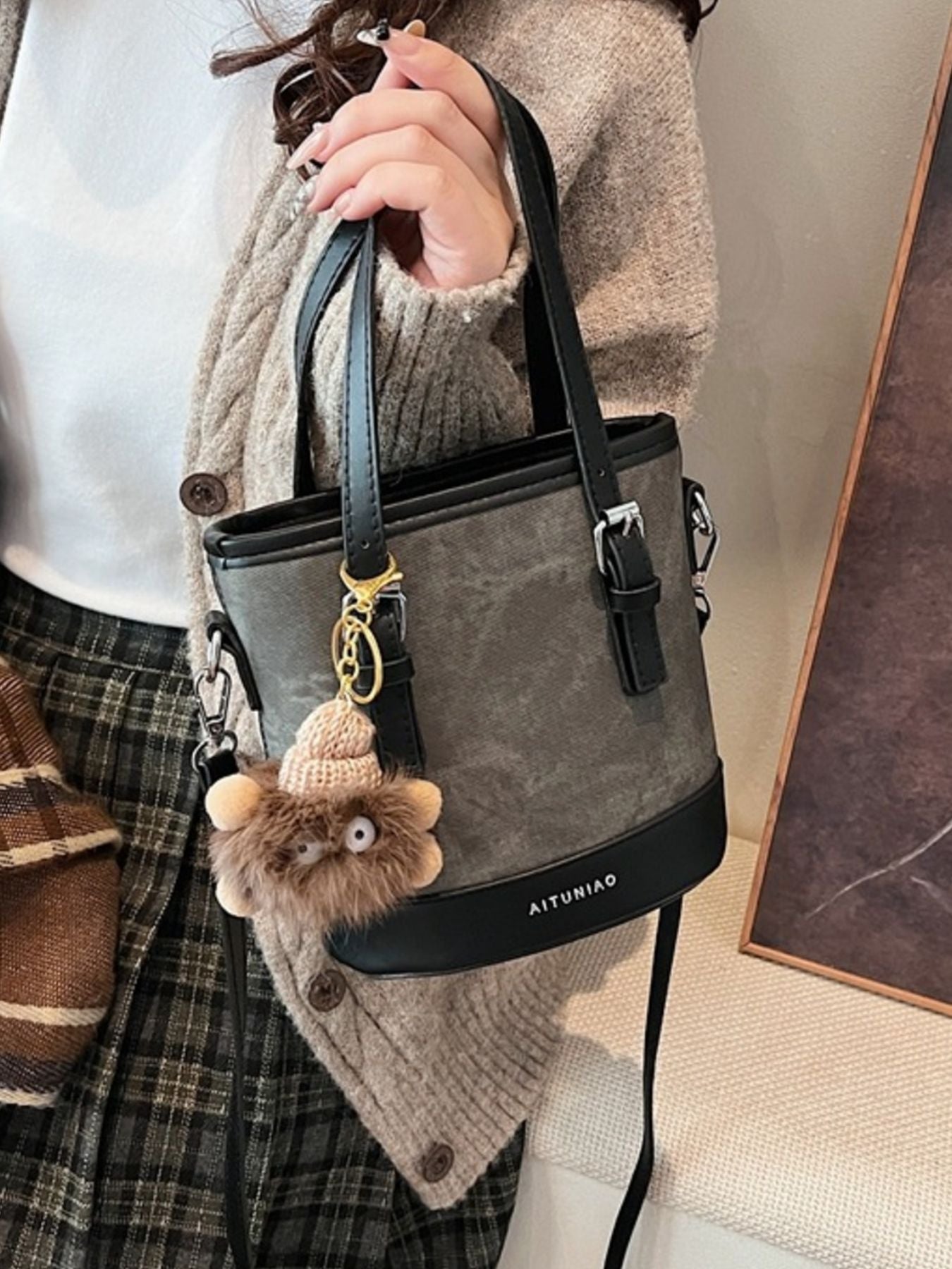 Premium two-tone bucket crossbody bag in gray canvas with black trim and a fuzzy charm.