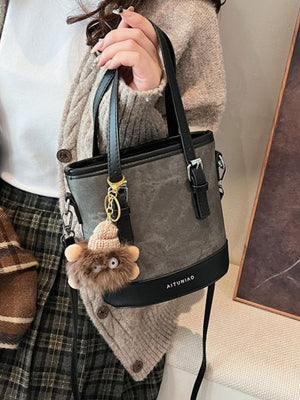 Premium two-tone bucket crossbody bag in gray canvas with black trim and a fuzzy charm.