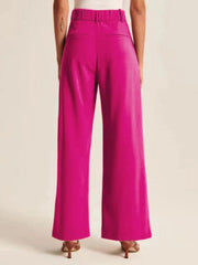 Magenta pleated palazzo trousers with a wide leg and elastic waistband, styled with heels.