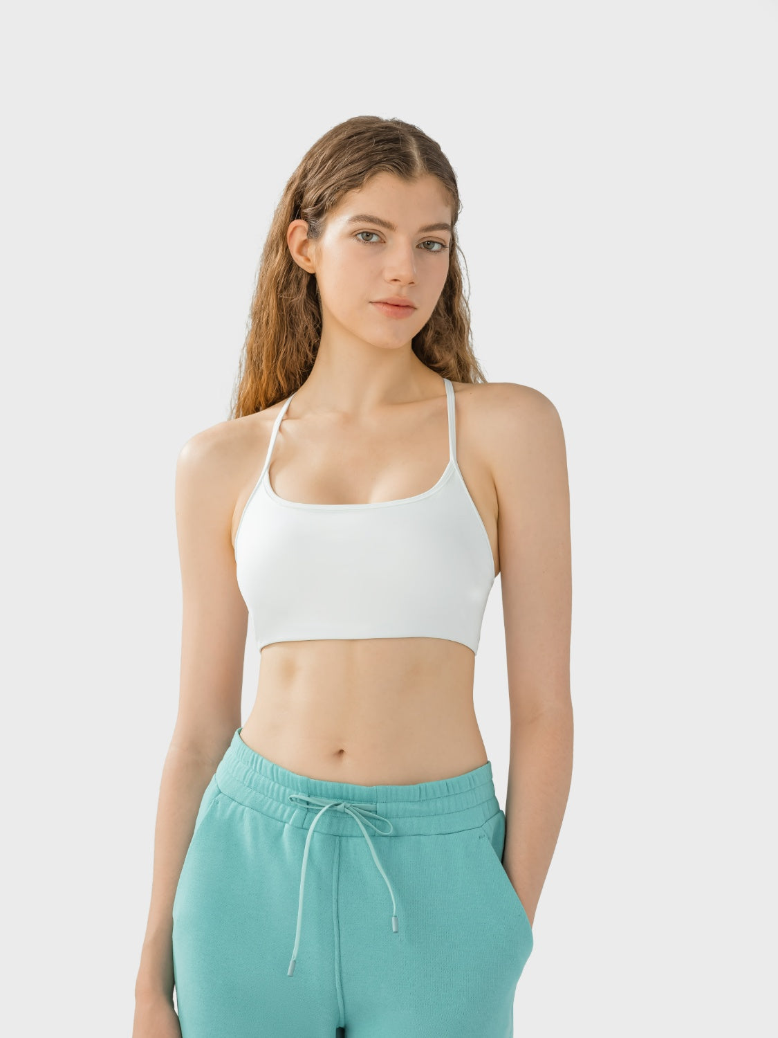 White active crop top with strappy back detail, paired with teal sweatpants.