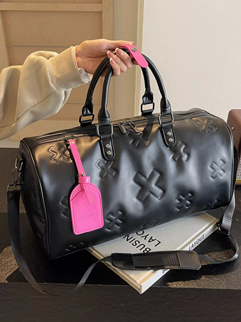 Black embossed cross detail luxury duffel bag with pink tag and strap.
