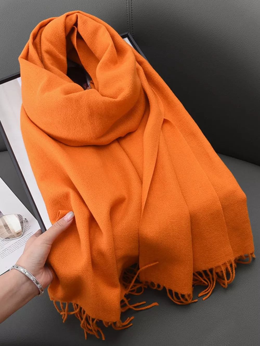 Orange fringed scarf with a soft texture, styled loosely.