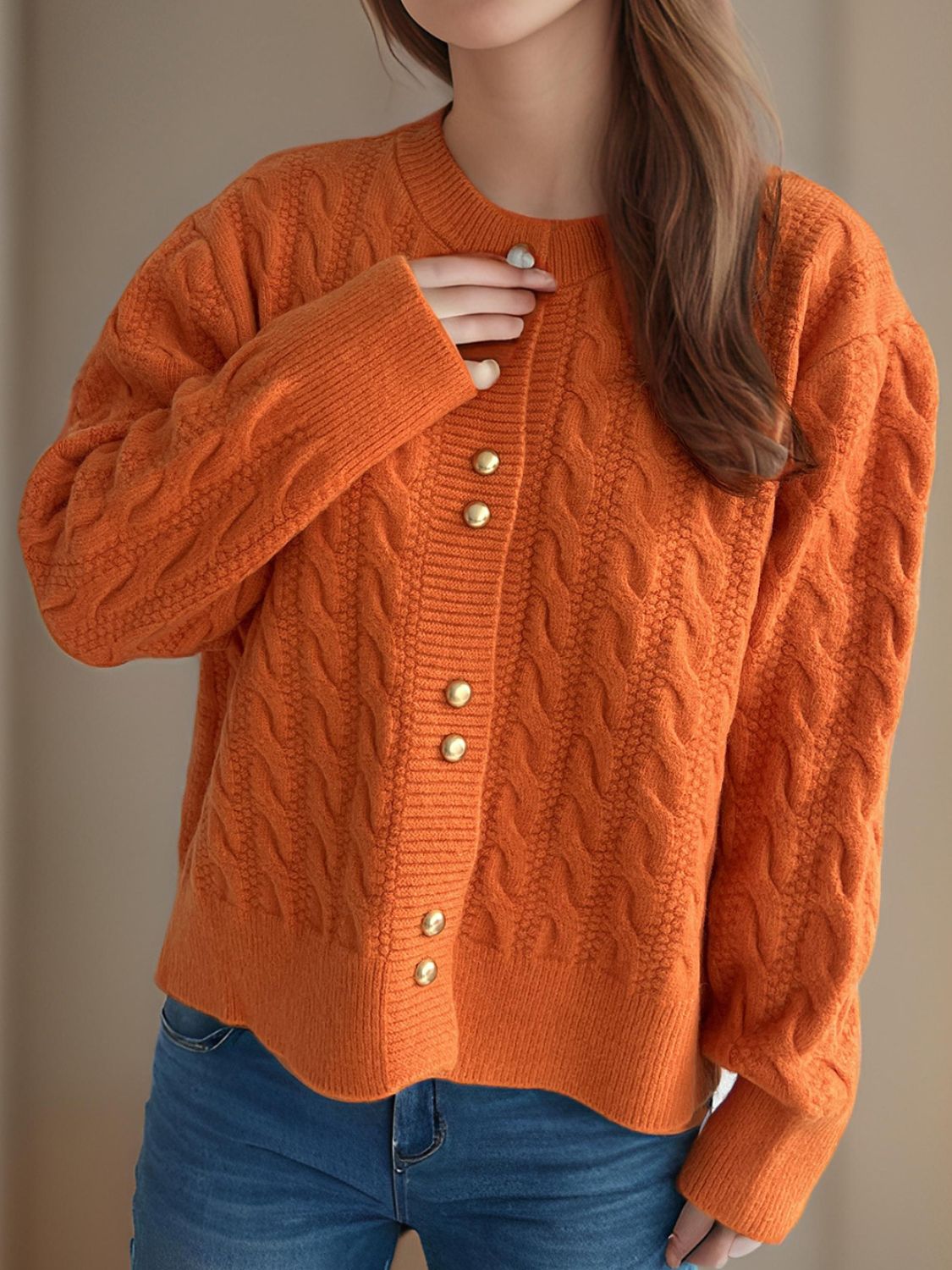 Orange cable knit cardigan with puff sleeves and gold buttons.