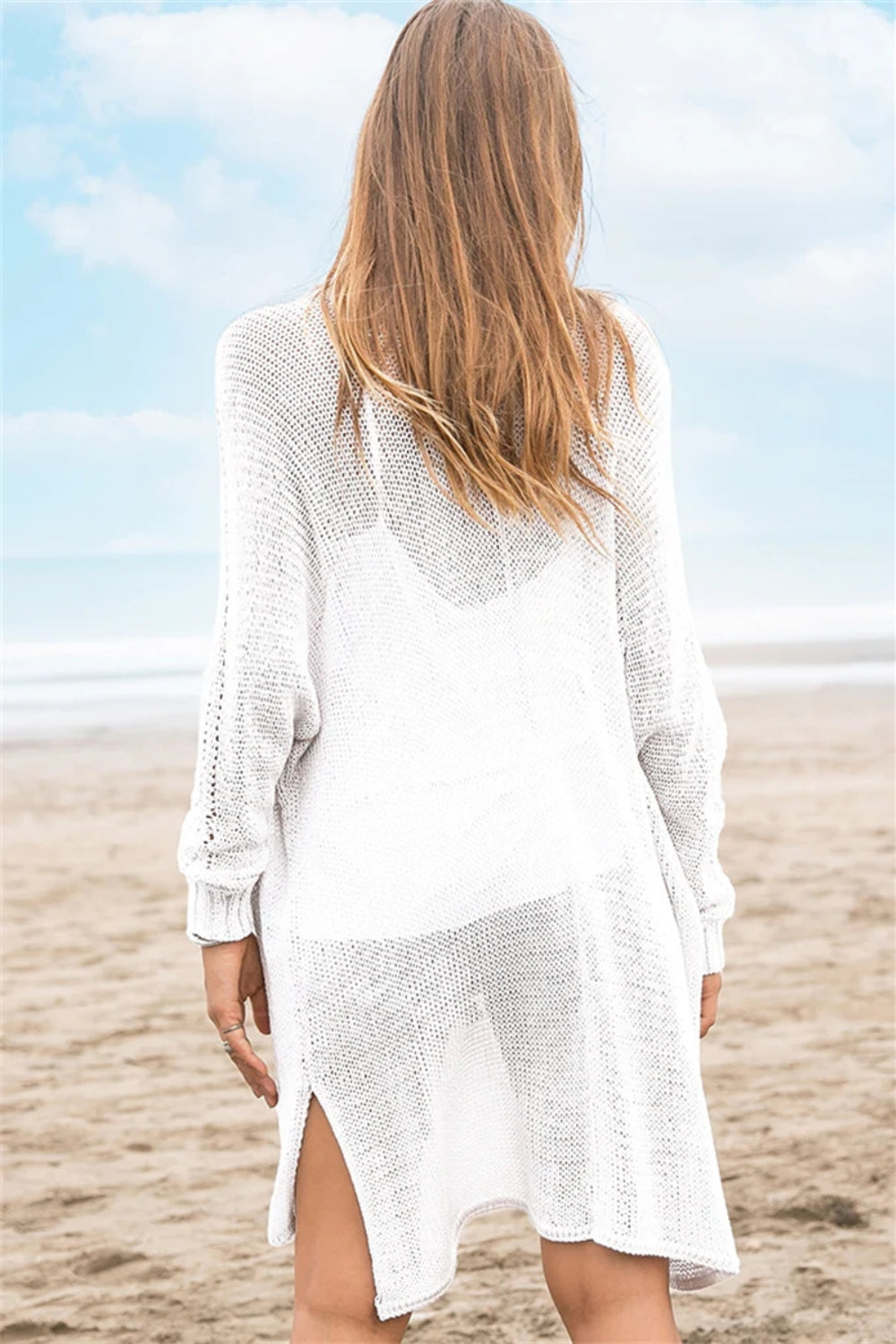 White open-knit acrylic cardigan with slit hem and long sleeves, worn over a tank top.