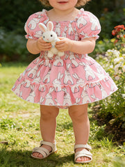 Pink bunny print baby dress with smocked bodice and ruffled hem, puff sleeves.