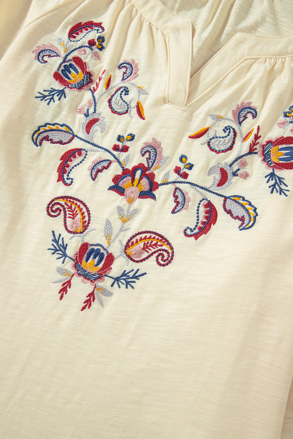 Pastel yellow blouse with colorful floral embroidery and V-neckline.