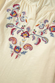 Pastel yellow blouse with colorful floral embroidery and V-neckline.