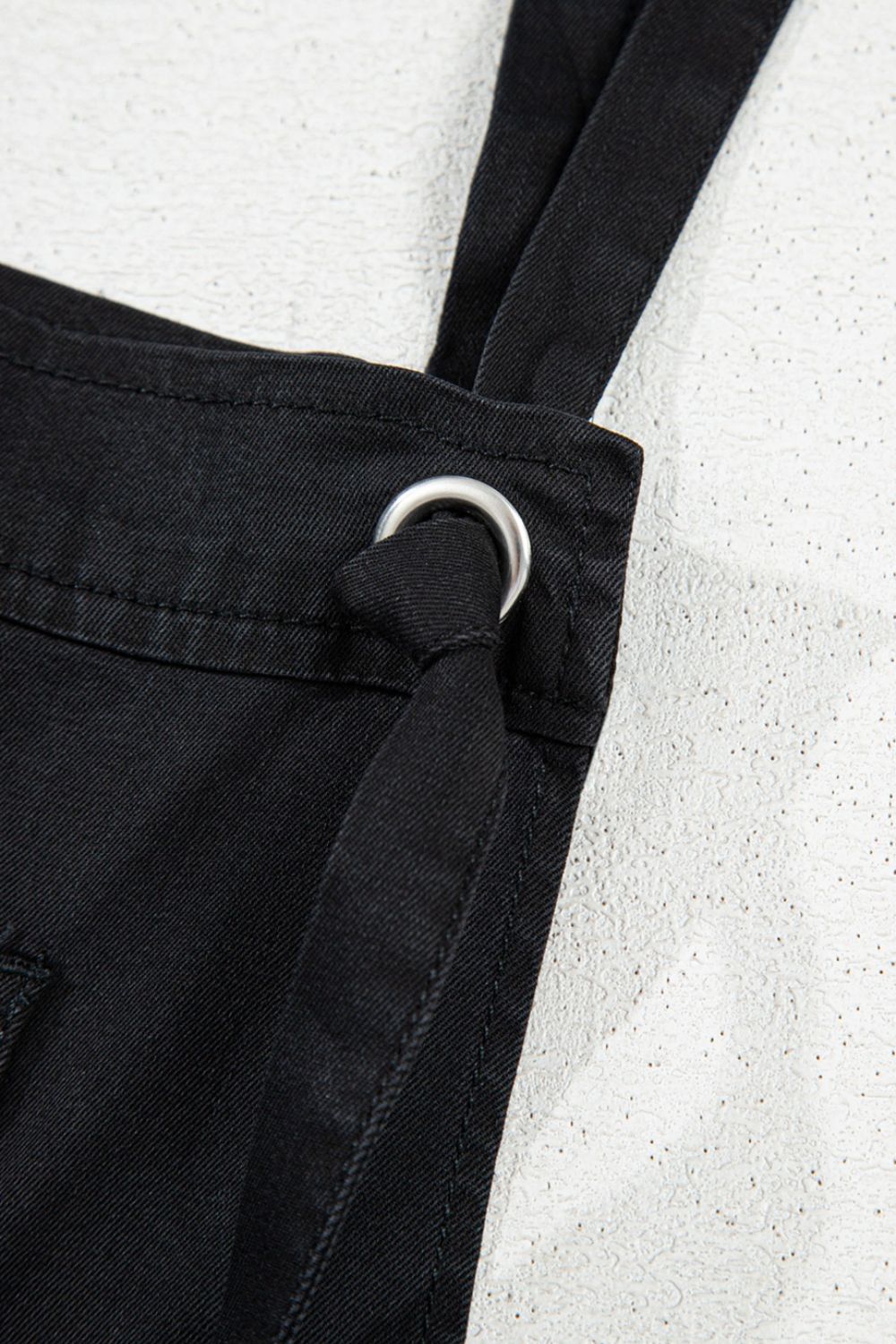 Black denim romper with adjustable straps and metal ring detail