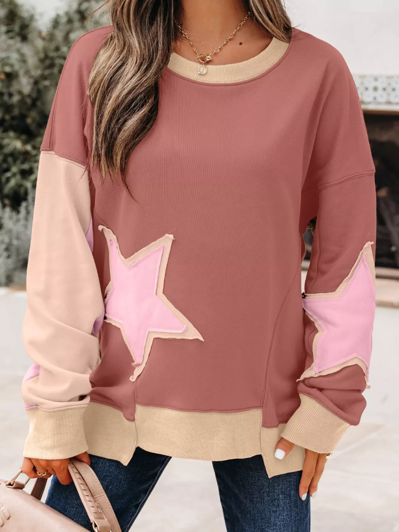 Dusty pink sweatshirt with contrast star patchwork and exposed seams.