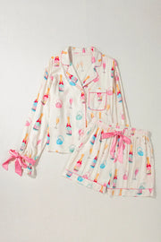 White silk pajama set with champagne print, pink piping, and bow details on sleeves and shorts.