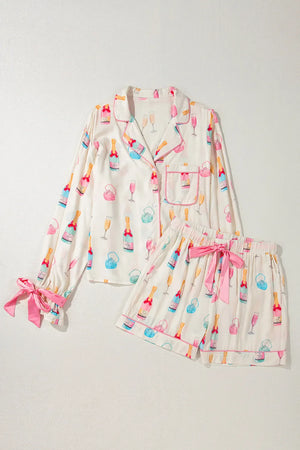 White silk pajama set with champagne print, pink piping, and bow details on sleeves and shorts.