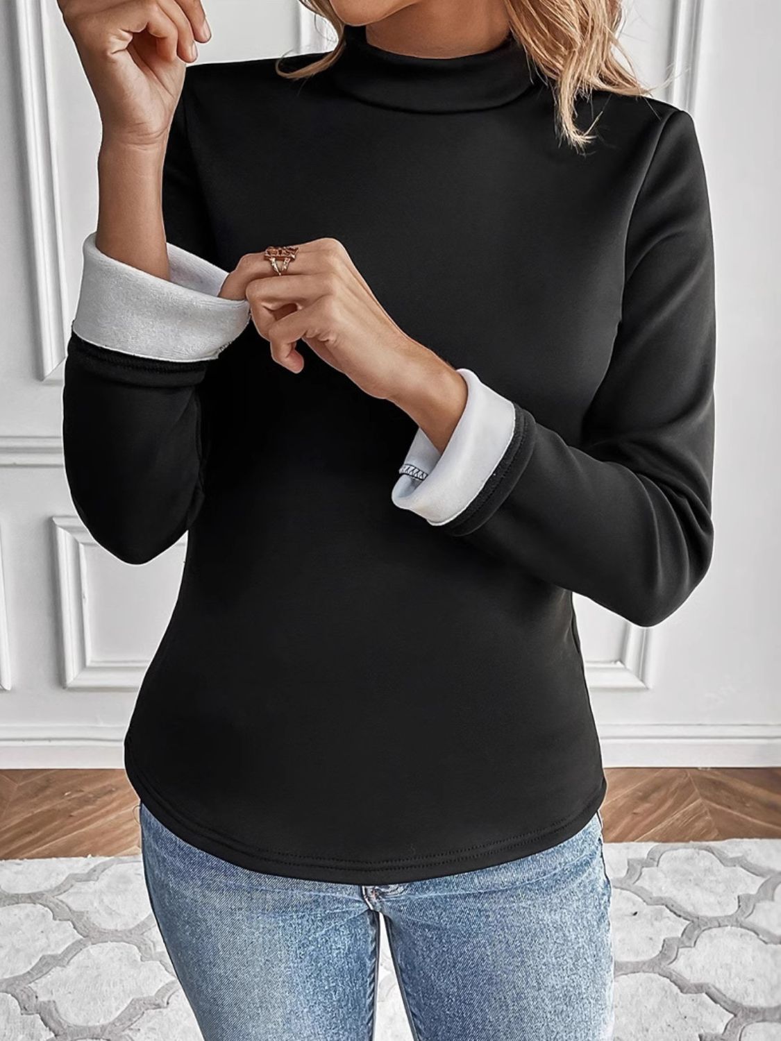 Black turtleneck sweater with reversible white cuffs and a curved hem.