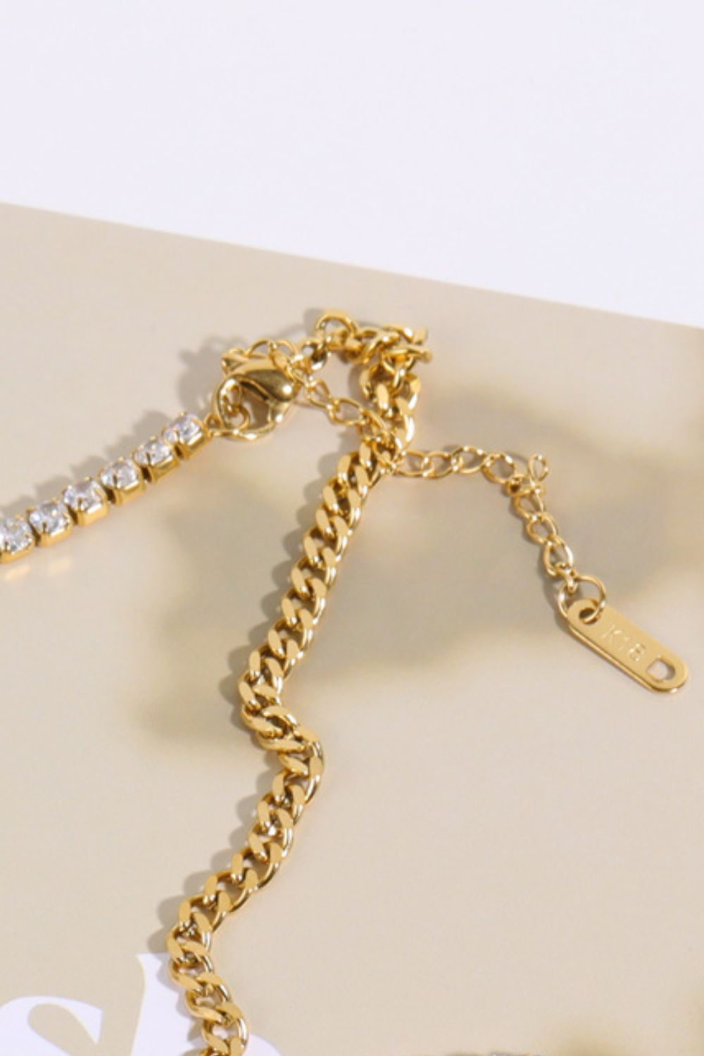 Gold curb chain necklace with a row of clear cubic zirconia stones and a lobster clasp closure.