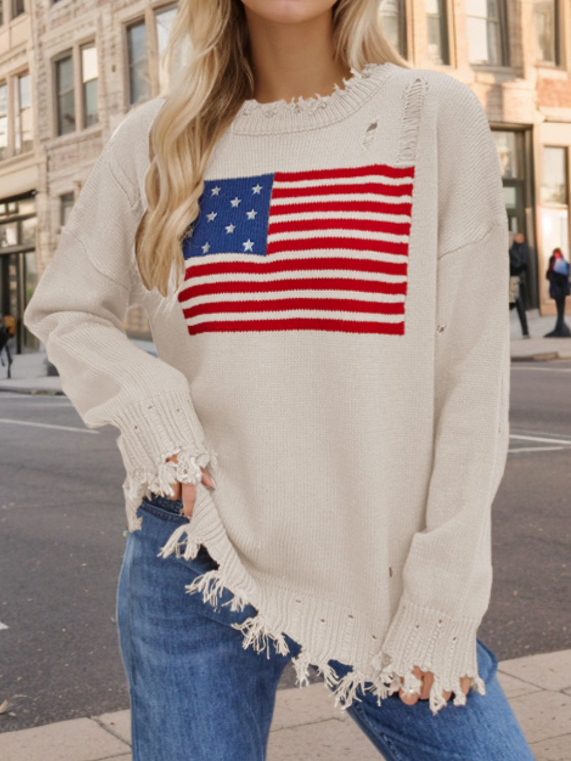 Cream knit sweater with distressed American flag graphic and frayed hem.