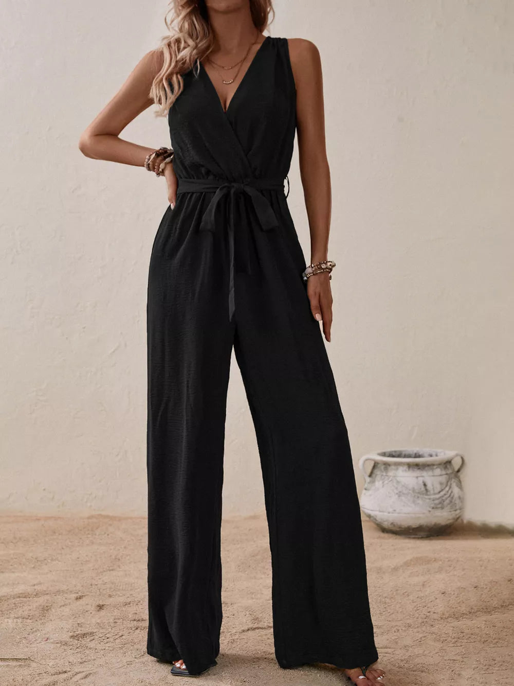 Black V-neck tie-waist wide-leg romper with sleeveless design and textured fabric.