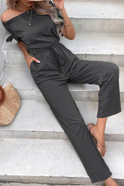 Off-the-shoulder jumpsuit in dark gray with tie sleeves, drawstring waist, and pockets.