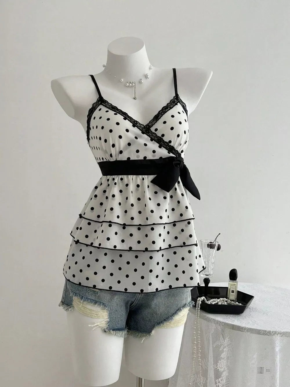 White polka dot camisole with black lace trim, tiered ruffles, and black bow detail.