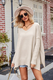 Beige knit sweater with V-neck, asymmetric hemline, and ribbed sleeves.
