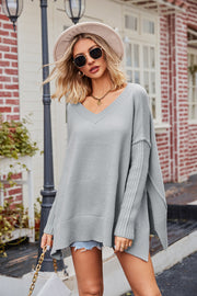 Gray knit sweater with V-neck, asymmetric hemline, and ribbed sleeves.