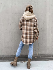 Oversized plaid shacket with attached hood in beige and brown, worn with jeans.