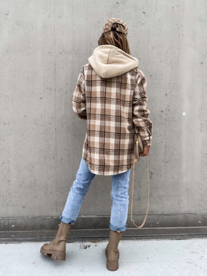 Oversized plaid shacket with attached hood in beige and brown, worn with jeans.