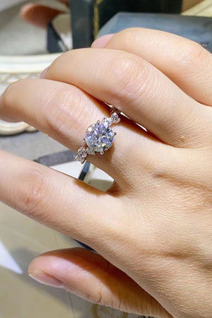 Silver moissanite halo ring with a central round-cut stone and delicate side accents.