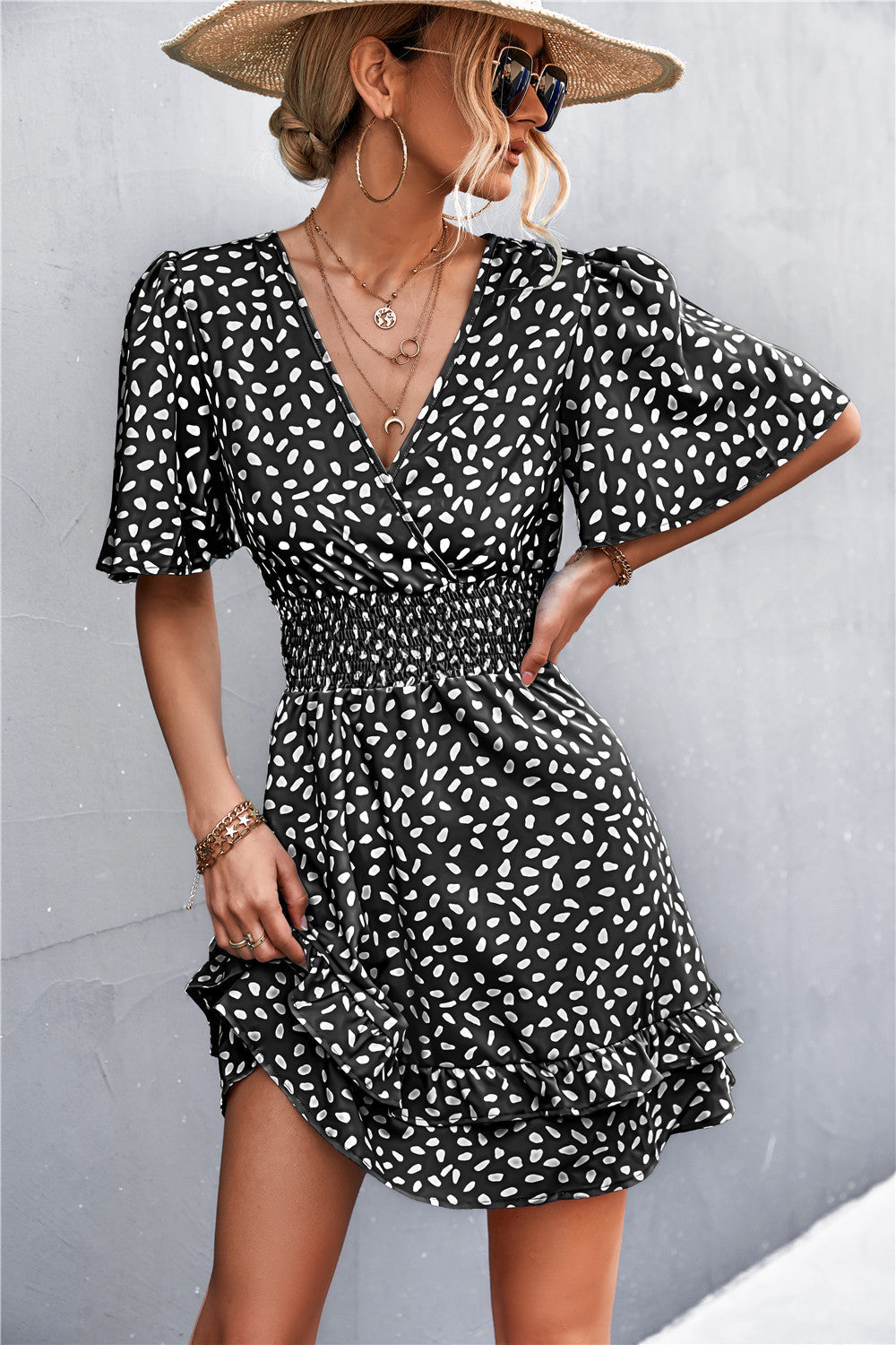 Black smocked waist mini dress with white speckle print, flutter sleeves, and ruffled hem.