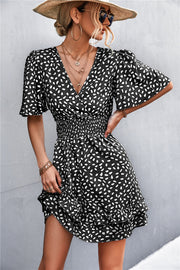 Black smocked waist mini dress with white speckle print, flutter sleeves, and ruffled hem.