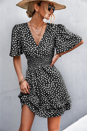 Black smocked waist mini dress with white speckle print, flutter sleeves, and ruffled hem.