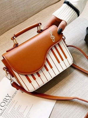 Brown and white piano key crossbody bag with a treble clef detail.