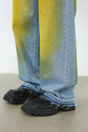 Oversized denim jeans in medium wash with yellow spray paint effect and frayed hems.