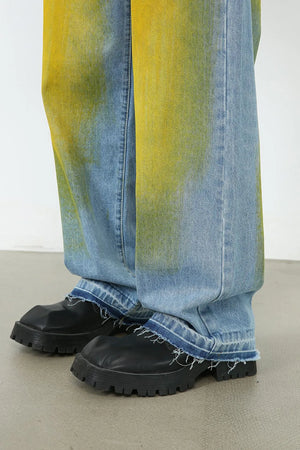 Oversized denim jeans in medium wash with yellow spray paint effect and frayed hems.