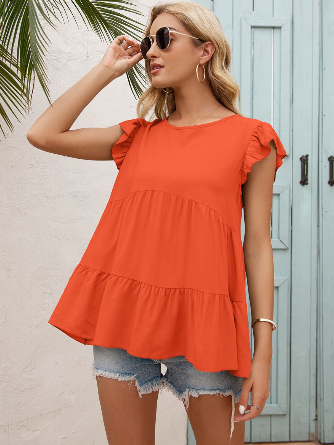 Orange ruffled yoke babydoll blouse with tiered hem and flutter sleeves.