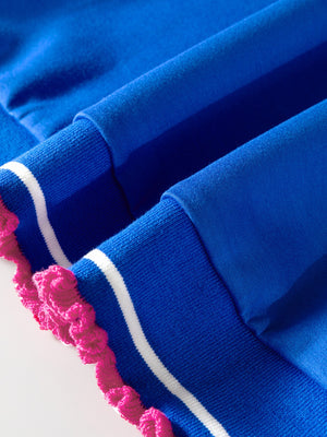 Blue polo shirt with white stripes and pink frill trim on the cuffs.