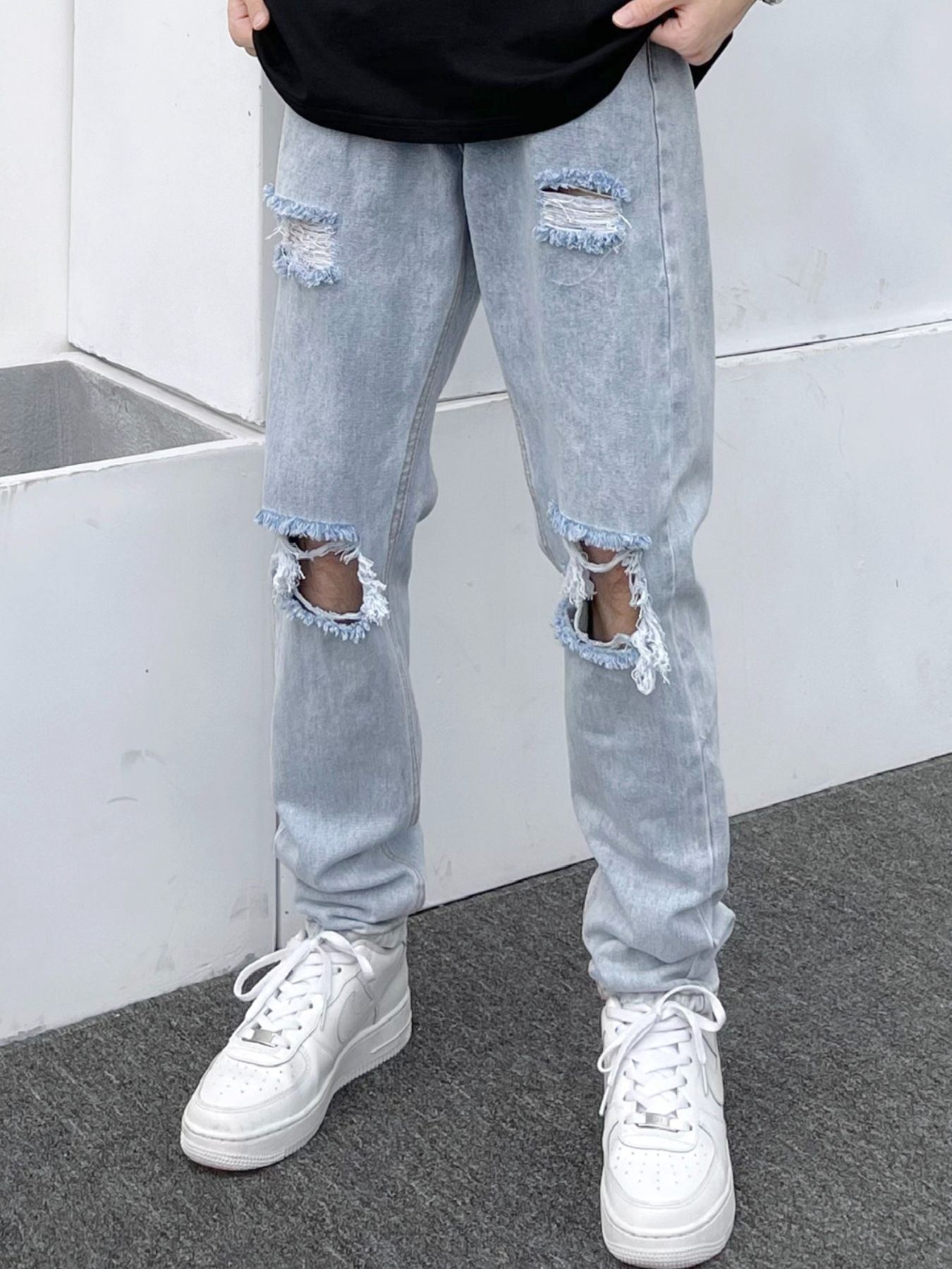 Light blue distressed slim fit men's jeans with ripped knees and frayed hems.