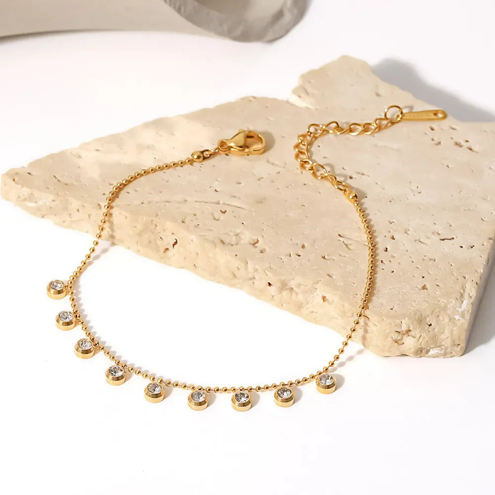 Gold bracelet with dangling zirconia beads and a beaded chain.