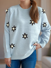 Pastel blue knit sweater with embroidered floral details and pom-poms.
