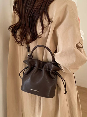 Brown pu leather cinch-top crossbody bag with knotted handle and drawstring closure.