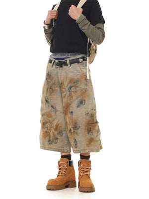 Men's wide-leg denim shorts in vintage wash beige with brown and black distressed details.