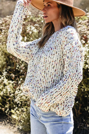 White confetti knit sweater with boatneck and long sleeves, styled with jeans.