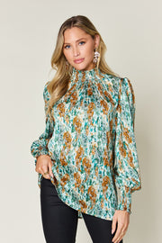 High neck abstract print blouse in green with smocked neckline and cuffs.
