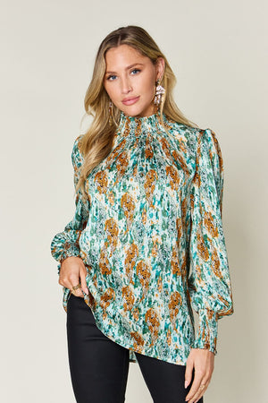 High neck abstract print blouse in green with smocked neckline and cuffs.